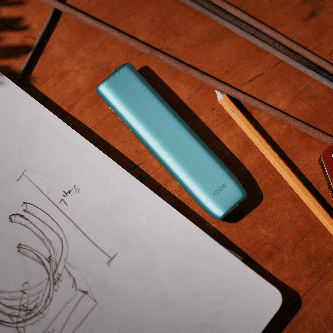 IQOS ILUMA i ONE color Breeze Blue next to a drawing and a Pencil